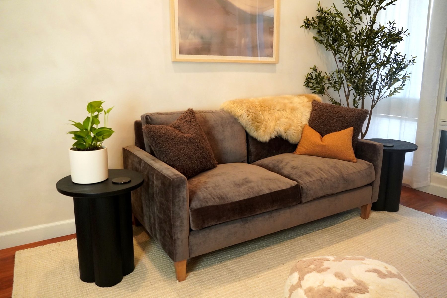 Velvet loveseat with sheepskin throw, sheltered between two black side tables and a tall olive tree.